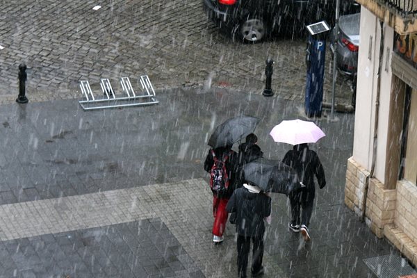 С чадъри и дъждобрани минувачите се пазят от мокрия сняг.