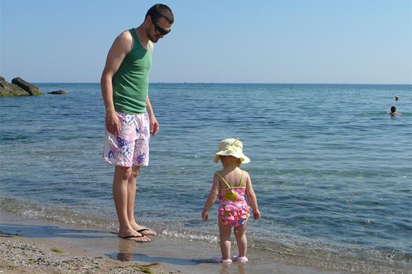 Таткото разхожда дъщеря си на брега на морето.
