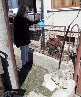 Социален служител подава на възрастна жена в Банско пакет с храни.