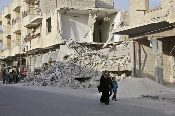 Сирийци вървят до разрушена сграда в Идлиб.