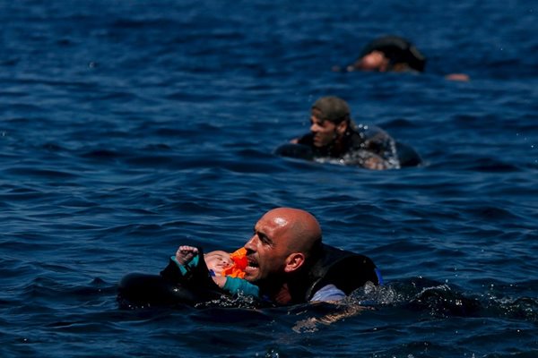 Сирийски бежанец носи бебе на ръцете си, след като се е преобърнала на 100 метра от гръцкия бряг/Септември