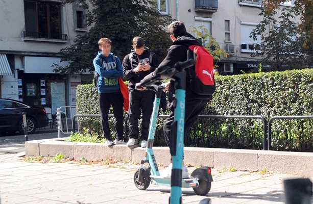 Младеж си говори по телефона, докато управлява електрическата тротинетка