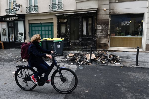 Жена минава с колело покрай изгорени от  протестиращи боклуци в Париж. СНИМКА: РОЙТЕРС