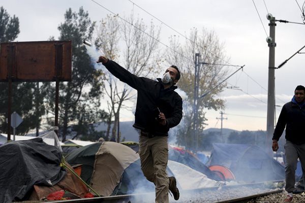 Мигрант хвърля към македонските полицаи бутилка със сълзотворен газ по време на сблъсъците на границата с Гърция.