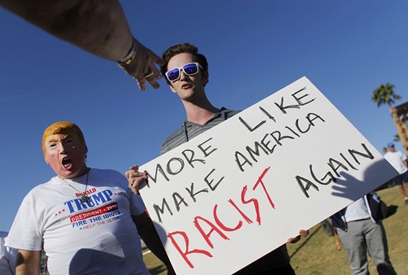 Противник на Доналд Тръмп държи плакат с надпис: “Много вероятно е той да направи Америка отново расистка” до демонстрант с маска на кандидат-президента на САЩ