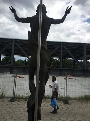 Пловдивчанин минава покрай статуята на Христос, който е разперил ръце и гледа към металната конструкция.