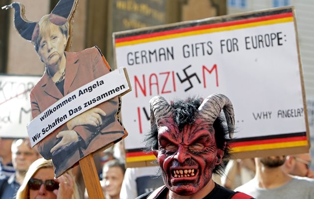 Мъж с маска на дявол в Прага държи плакат с думите “Добре дошла, Ангела, заедно можем да го направим”. Протестиращите срещу германския канцлер парадират популярната реплика на Меркел “заедно ще се справим” с наплива от бежанци.