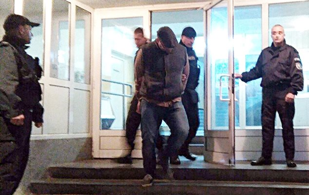 Полицаи извеждат Божо от сградата на ОДМВР в Бургас. Той крие лицето си под козирката на каскет. Снимка: Елена Фотева