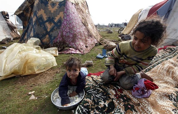 Бебе яде ориз в сирийски бежански лагер, докато по-голямата му сестра се грижи за него до импровизирана палатката в град Вирансехир, Югоизточна Турция