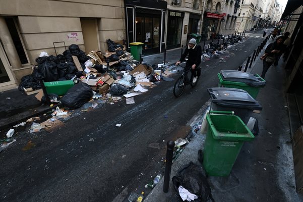 Мъж с колело минава по пълна с боклуци улица в Париж.