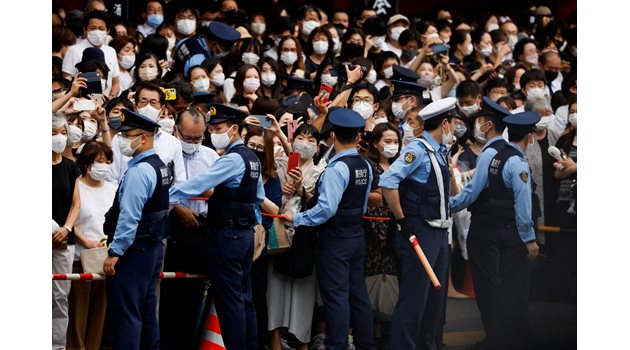 Полицейски служители стоят на стража, докато хората наблюдават кортеж, превозващ тялото на покойния бивш японски премиер Шиндзо Абе
