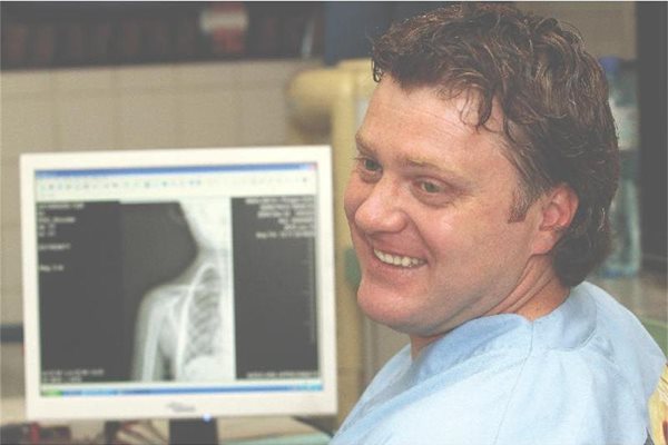 Д-р Кацаров с усмивка обяснява на пациент какво вижда на снимката на ръката му.