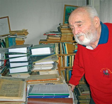 Акад. Кирил Василев пред отрупаното с книги и бележницио бюро в кабинета си през 2012 г. 
СНИМКА: АВТОРЪТ