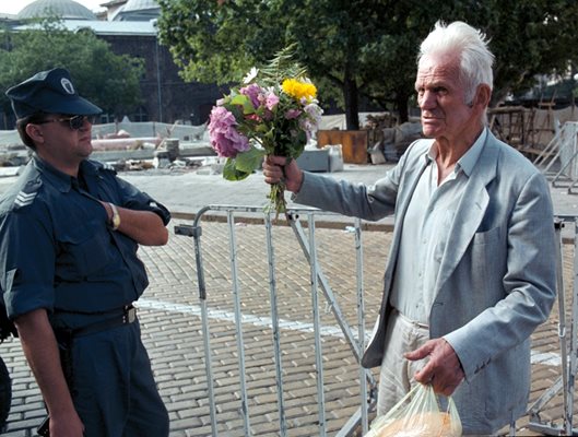 Възрастен мъж носи цветя, които иска да остави на мястото на мавзолея.