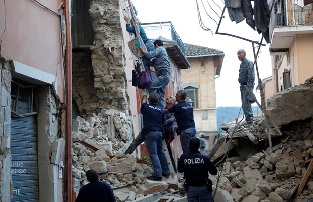 Полицаи и доброволци помагат на жена да излезе по стълба от унищожения си дом.