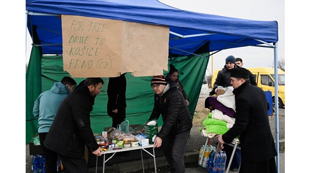 Доброволци подреждат храна, напитки и одеяла за бежанци, които пристигат от Украйна в Словакия. Голям надпис на различни езици гласи: “Безплатно”.