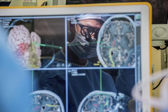 Неврохирургът д-р Едуард Чанг се вижда като отражение на компютърен монитор, показващ мозъчни сканирания, докато прави операция в UCSF. Снимката е от 2017 година. Снимка: Калифорнийски университет