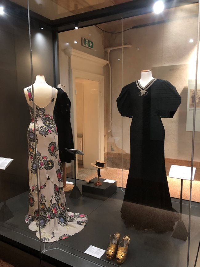 Светлата вечерна рокля с флорални мотиви вероятно е вдъхновена от модел на Елза Скиапарели. Тъмната рокля е с буфан ръкави.
