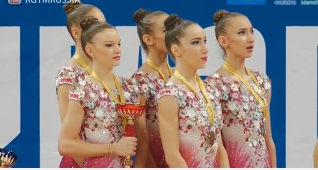 Момичетата от новия ансамбъл на България за жени пеят химна, докато гледат как родният трибагреник се издига над знамето на Русия в Москва.