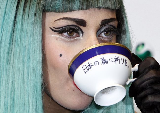 Певицата пие чай от чаша, на която пише “Молете се за Япония”. Тя участва в благотворителен концерт за жертвите на труса от 2011 г.