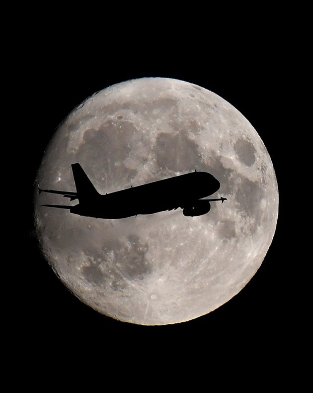 Пътнически самолет преминава през диска на Луната на летище Хийтроу, Лондон